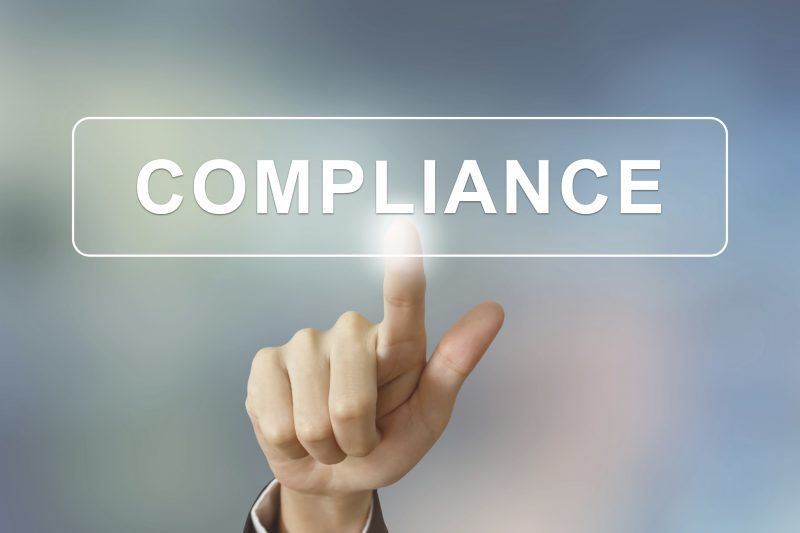 business hand pushing compliance button on blurred background