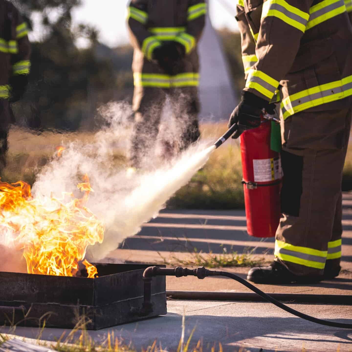 Firefighters using a fire extinguisher to put out a controlled fire outdoors, emphasising fire safety and prevention measures.