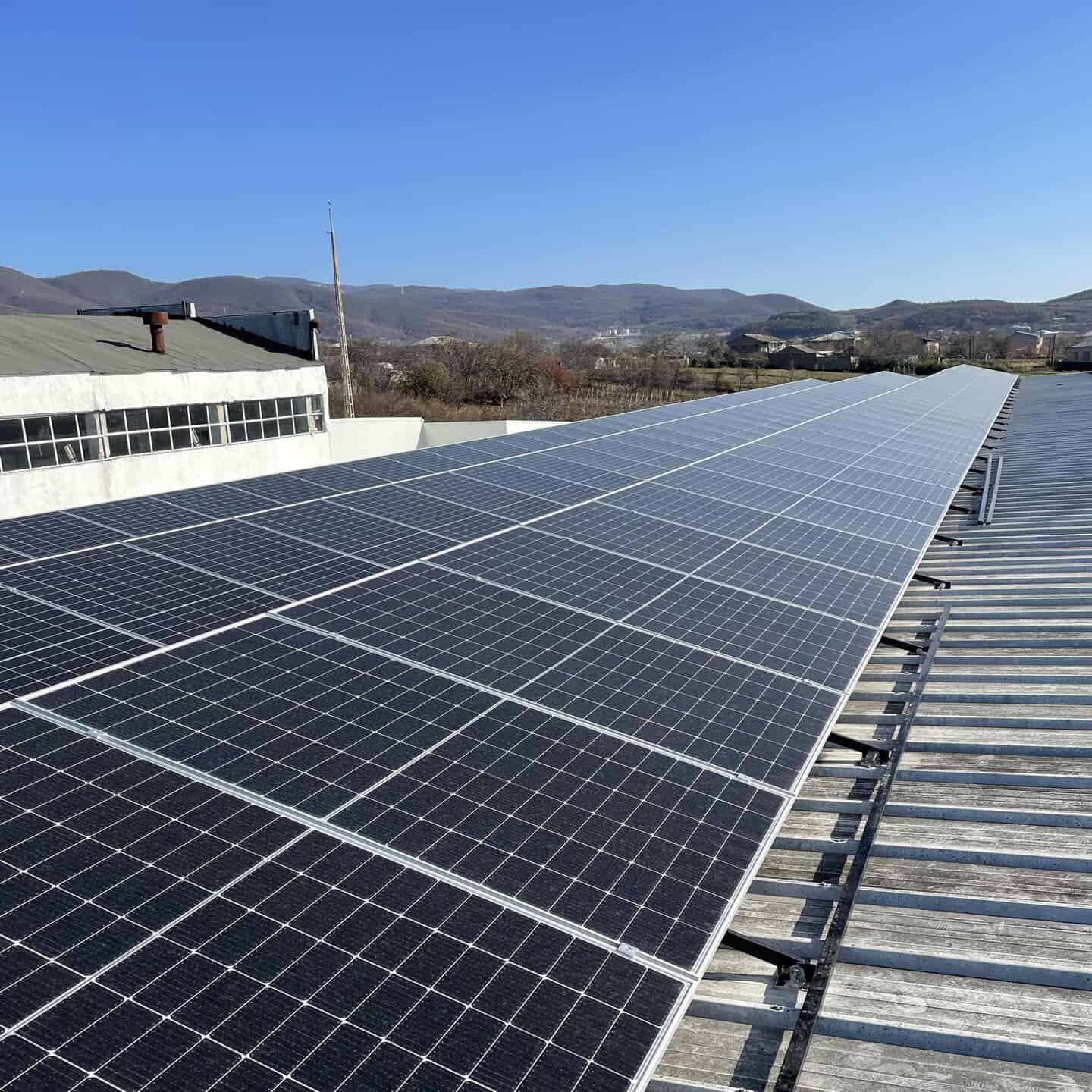 Commercial rooftop solar panel installation on a large commercial building, with rows of photovoltaic panels mounted across the flat roof under daylight conditions.